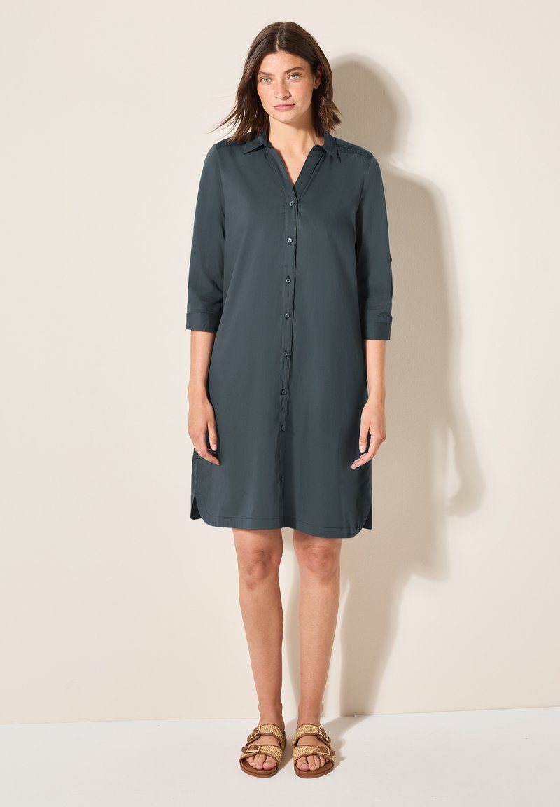 Abito camicia di colore grigio scuro, realizzato in tessuto morbido, con colletto, maniche a tre quarti e spacchi laterali all'orlo.