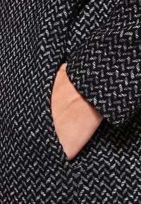 Černo-bílá vzorovaná látka s geometrickým designem, obsahující boční kapsu. Textura vypadá jako pletená a hustá.