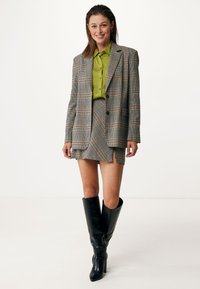 Blazer a quadri grigio con dettagli arancioni e blu, abbinato a una camicia verde button-up, una mini gonna a quadri e stivali neri al ginocchio.
