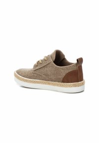 Zapatilla de tela beige con un acento de cuero marrón, suela de goma blanca y borde de yute. Presenta una punta redondeada y diseño con cordones.