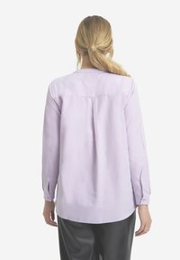 Jasnofioletowa koszula z długim rękawem, z plisą z tyłu, zapinanymi mankietami i zaokrąglonym dołem, wykonana z gładkiego materiału.