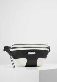 Mustekka ja valkoinen vyölaukku vetoketjulla, jossa on sileä pinta, kontrastivalkoiset yksityiskohdat ja logo "KARL" valkoisena.