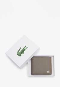 Portafoglio in pelle grigia all'interno di una scatola bianca con un logo di coccodrillo verde sul coperchio. Texture liscia, forma rettangolare, design minimalista.