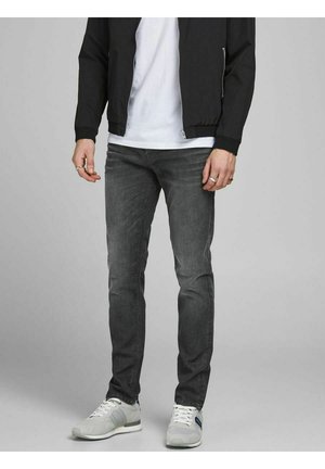 Graue Denim-Jeans mit Slim-Fit, einem subtilen Washed-Effekt, im fünf Taschen Design, kombiniert mit weißen Sneakers und einer schwarzen Bomberjacke.