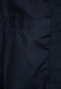 Tessuto blu navy con una texture liscia, dotato di una cucitura laterale e un discreto dettaglio della tasca. Accenti di cucitura minima, colore uniforme.