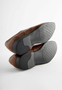 Chaussures en cuir marron avec une surface lisse, des coutures décoratives et des semelles en caoutchouc noir dotées d'un motif de grip texturé.