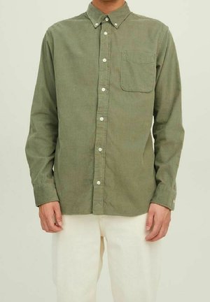 Olivgrünes Hemd mit Knopfleiste aus einem weichen, strukturierten Stoff, mit einer einzelnen Brusttasche und weißen Knöpfen, getragen zu hellen Hosen.