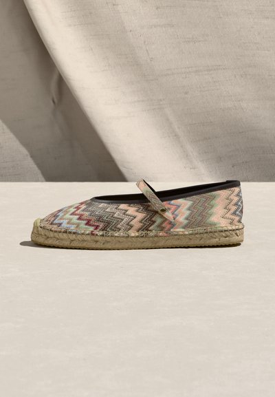 Επίπεδη εσπαντρίγια με πολύχρωμο ζιγκ ζαγκ μοτίβο, μαύρο περίγραμμα και λεπτό λουράκι στην κορυφή, τοποθετημένη πάνω σε μπεζ υφασμάτινο φόντο.