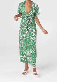 Maxi-jurk in het groen met witte bloemenprint, korte mouwen, een strik in de taille en een diepe V-halslijn. Draag met witte sandalen met bandjes.