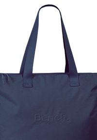 Navyblauwe schoudertas van duurzaam materiaal; heeft lange schouderbanden en een reliëflogo. Eenvoudig, plat ontwerp zonder extra patronen.