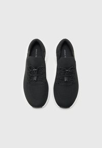 Baskets en tricot noires avec un dessus texturé, dotées de lacets élastiques et d'une semelle blanche. Conception légère avec un style à enfiler.