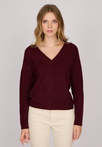 Pull en tricot bordeaux avec un col en V, coupe ample et manches longues. La texture semble douce, idéale pour les superpositions.