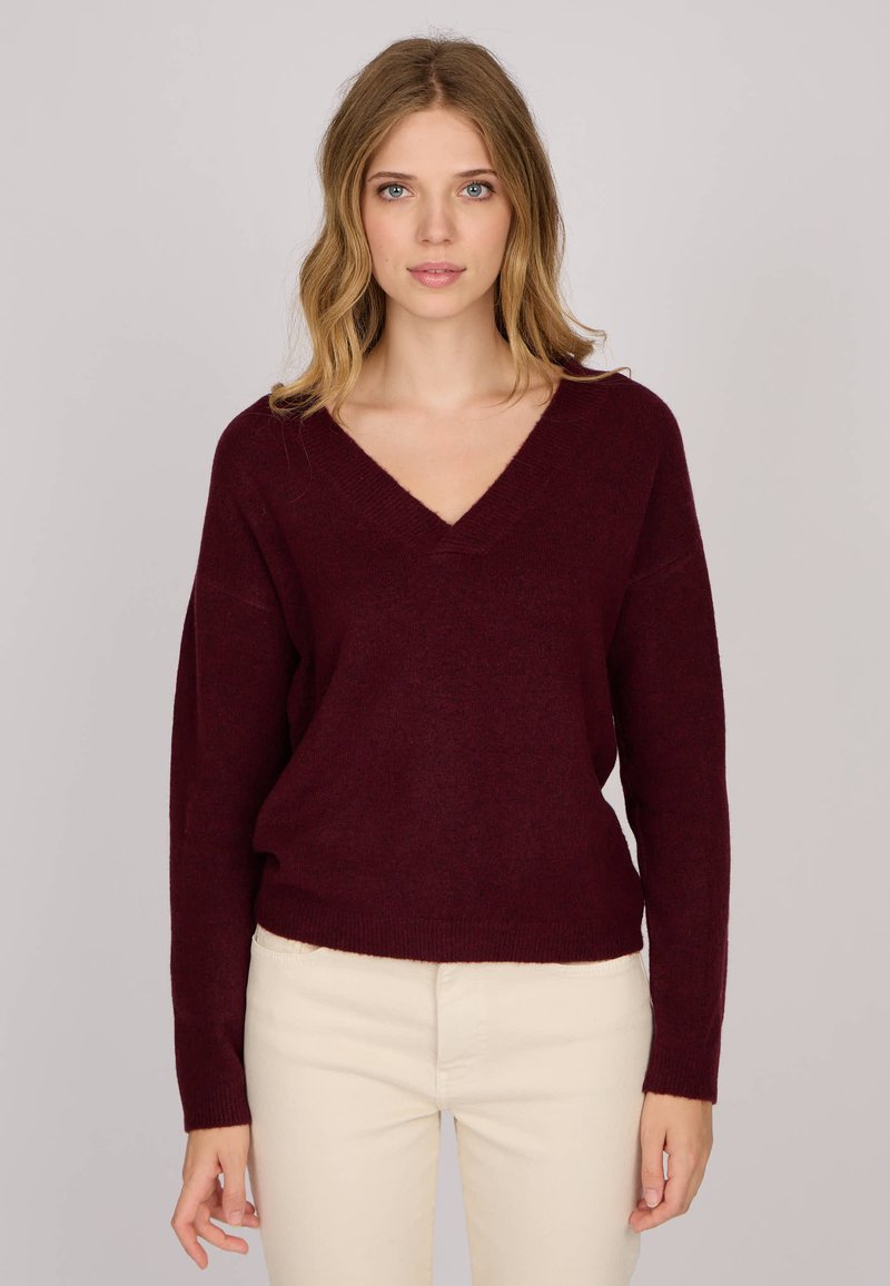 Pull en tricot bordeaux avec un col en V, coupe ample et manches longues. La texture semble douce, idéale pour les superpositions.