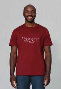 Bordeauxkleurig katoenen T-shirt met korte mouwen, featuring witte tekst met de zin "Das ist aber ein schöner Baum." Crew neck ontwerp, standaard pasvorm.