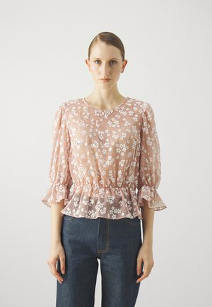 Light pink blouse with white floral pattern, ruffled sleeves, and peplum waist. Worn with dark denim jeans, featuring a high waist and straight cut.