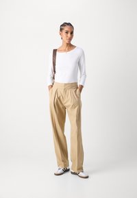 Top blanco de manga larga con escote redondo, pantalones beige con pliegues y zapatillas blancas con rayas negras. Fondo claro.