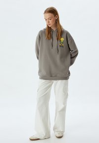 Sudadera gris con cordón y un gráfico de Tweety Bird. Combinada con pantalones cargo de pierna ancha blancos y zapatos beige. Textura suave.