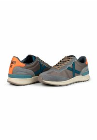 Zapatillas grises y marrones de malla y ante, con detalles azules, un talón de color naranja brillante y suelas beiges. Texto en el talón.