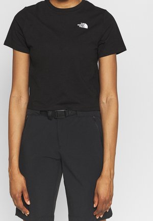 Osoba ubrana w czarny krótki t-shirt North Face oraz czarne szorty z paskiem na jednolitym jasnym tle.