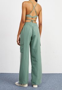 Grüne Cargo-Hosen mit lockerer Passform, elastischem Bund, seitlichen Taschen und kontrastierenden vertikalen Streifen. Getragen mit einem passenden Trägershirt.