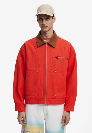 Red fabric jacket with a brown collar, front zipper, two large pockets, and a small zipped pocket on the chest; smooth texture.