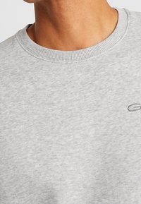 Grijze sweatshirt met een gestructureerde, zachte stof. Voorzien van een ronde hals en een subtiel geborduurd logo op de borst.