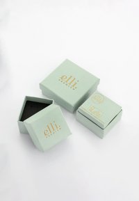 Scatole verde menta con scritte dorate, una quadrata e due esagonali, con un interno nero. Il design presenta un aspetto pulito e moderno.