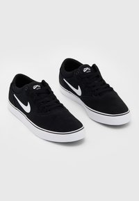 Black suede sneakers with white accents, featuring a white Nike Swoosh logo, black laces, and a white rubber sole with subtle detailing.