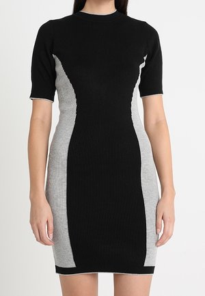Femme portant une robe à manches courtes en maille côtelée avec un centre noir et des panneaux latéraux gris, debout, les bras détendus le long du corps.