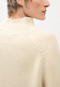 Beige bordázott kötött pulóver magas gallérral, textúrált anyaggal és laza illeszkedéssel, hátulról bemutatva, kiemelve a nyakkivágást.