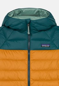 Izolirana puffer jakna koja ima gornji deo u tirkiznoj boji, donji deo u narandžastoj boji, visoki ovratnik i prednji rajsferšlus sa uzorčastim povlačnim držačem.