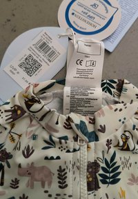 Musterlose Softshell-Babyjacke in hellcreme mit Tier- und Pflanzenmotiven. Reißverschluss vorne, elastische Bündchen und atmungsaktiver Stoff.