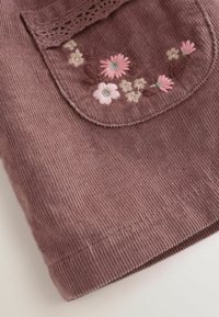 Close-up of mauve corduroy fabric with a flap pocket featuring pink and cream floral embroidery and lace trim.