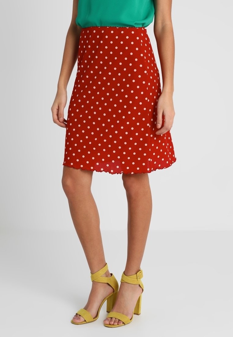 Czerwona spódnica w kropki z falbanym dołem, lekki materiał, zestawiona z zieloną górą i żółtymi sandałami na obcasie w klocku.