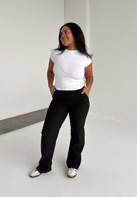 White short-sleeve fitted top, black high-waisted trousers, and white sneakers with brown accents, against a neutral background.