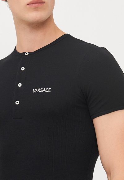 Schwarz geripptes Kurzarm-Henley-Shirt mit fünf weißen Knöpfen und "VERSACE"-Logo in weißer Stickerei auf der linken Brust.