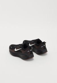 Black running shoes with a mesh upper, white Nike swoosh, patterned accents, and a cushioned sole featuring "zoomx" branding.