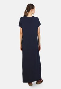 Abito maxi blu navy a maniche corte con silhouette ampia. Tessuto leggero e liscio che arriva fino alle caviglie. Abbinato a calzature casual.