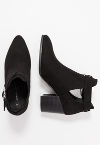 Ett par svarta mockakängor med blockklackar, spetsiga tår, sidoutskärning och ett band med spänne på vit bakgrund.