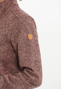 Fleece-pullover i vinröd med en strukturerad yta, som har en präglad läderlogo på vänster ärm och en hög krage.