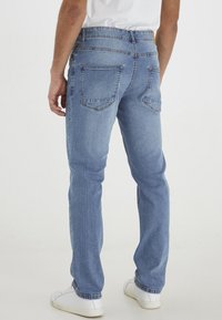 Izbalināti zila denima džinsi ar taisnu griezumu, divām aizmugurējām kabatām, nedaudz izsistām vietām un apakšmalu, kas beidzas tieši virs baltajiem sporta apaviem.