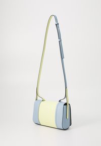 Pravilni pravokutni crossbody torba u svijetloplavoj i žutoj koži, s crnim detaljima. Sadrži uski podesivi remen i glatku teksturu.