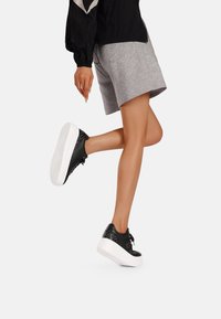 Sneaker in pelle nera con suole a piattaforma bianche, caratterizzate da borchie decorative sul tallone e chiusura con lacci neri.