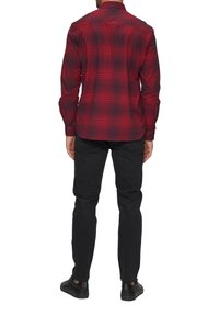 Rode en zwarte geblokte blouse met lange mouwen, een kraag, knoopmanchetten en een gebogen zoom, gedragen met zwarte pantalon en sneakers.