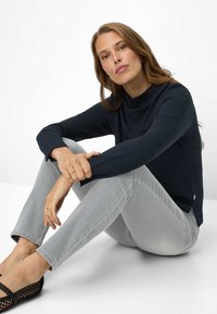 Top a maniche lunghe blu navy con collo alto a imbuto, abbinato a jeans skinny grigio chiaro e ballerine nere in mesh. Presenta uno spacco laterale nell'orlo.