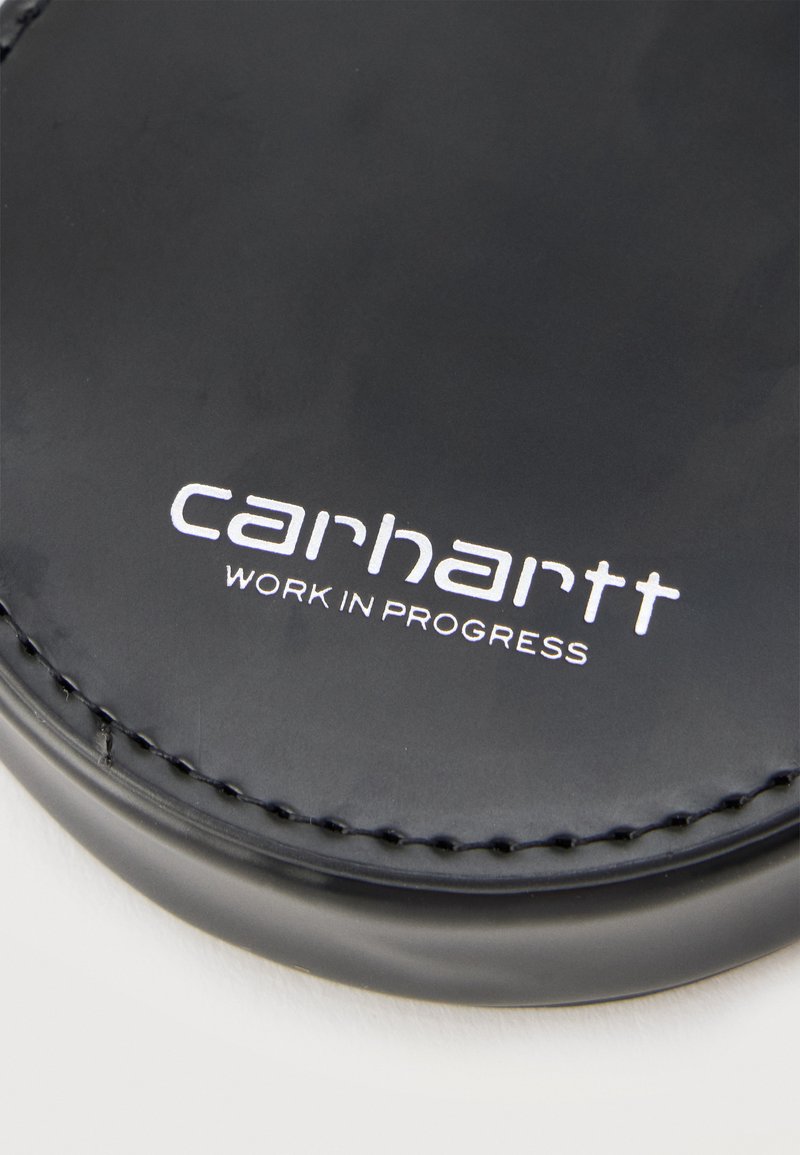 Gros plan d'un article en cuir noir avec le logo blanc « Carhartt Work In Progress » et des coutures détaillées sur le bord.