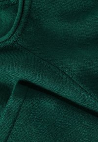 Țesătură tricotată de culoare verde închis, cu o textură moale, având detalii de coasere vizibile și o suprafață netedă. Fără modele sau accente vizibile.