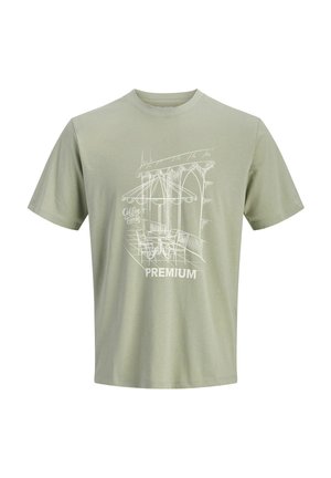 Camiseta verde claro con un dibujo en línea blanca de una escena de cafetería al aire libre, que incluye mesas, sillas, sombrilla y las palabras "Hora de Café" y "Premium".