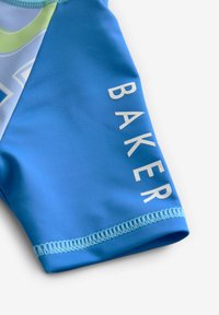 Modre kopalne hlače iz gladkega materiala, ki imajo diagonalne svetlo modre in zelene poudarke. Na hlačah je v belem tisku napisan "BAKER".