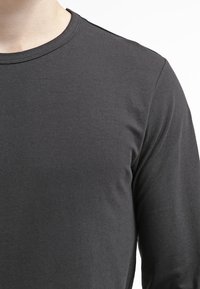 Pánská košile s dlouhým rukávem v tmavě šedé barvě, vyrobená z měkké bavlny, s kulatým výstřihem a hladkým povrchem, bez viditelných vzorů nebo akcentů.